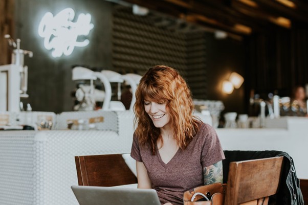 A smiling woman looking at a laptop in a cafe.